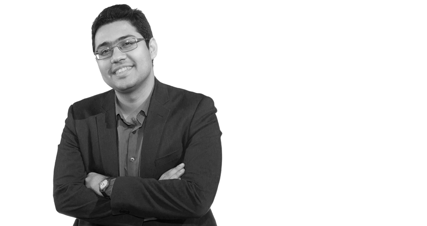 Smiling person in a suit jacket and glasses with arms crossed, against a white background.