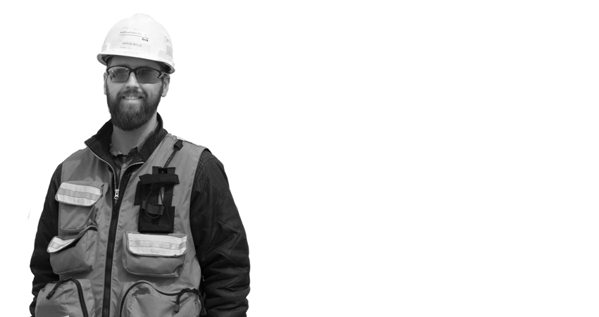 Man in safety vest and hard hat standing with a smile against a plain background.