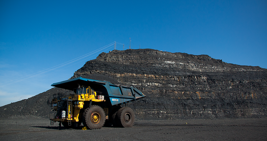 A large mining truck in front of a rocky hill under a clear blue sky.