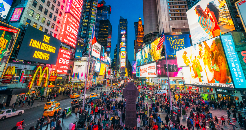 Times Square at evening; crowds, bright billboards, taxis, and skyscrapers fill the lively scene.