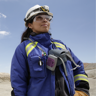 Worker in safety gear and helmet stands outdoors, looking ahead confidently under a clear sky.