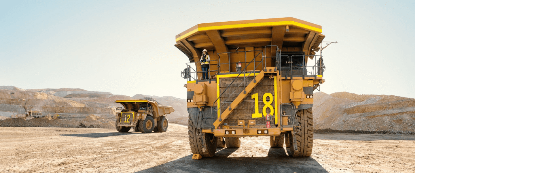 Two large yellow mining trucks in a quarry under a clear sky.
