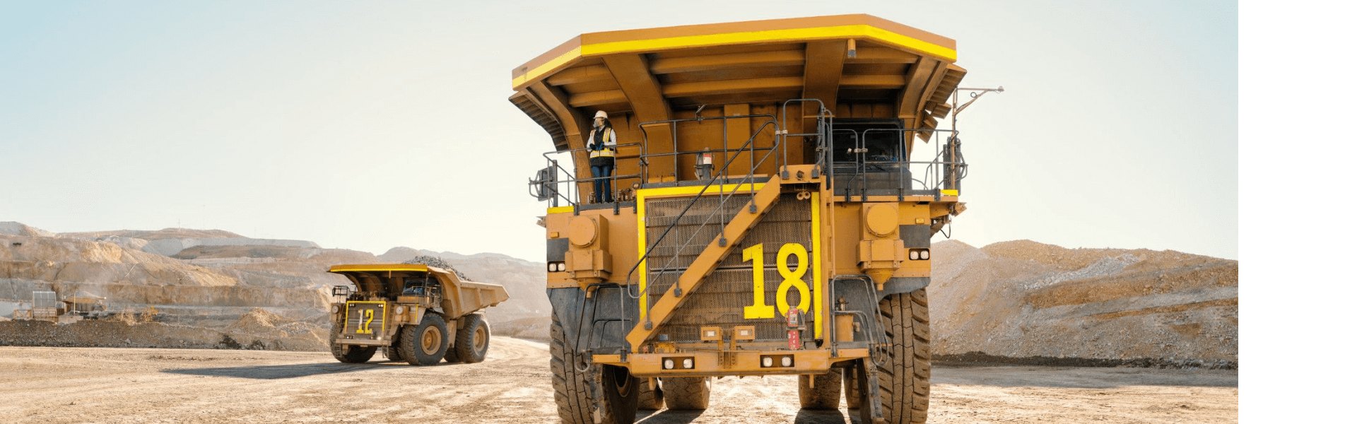 Large mining trucks in a quarry, with a worker standing on the front of truck number 18.