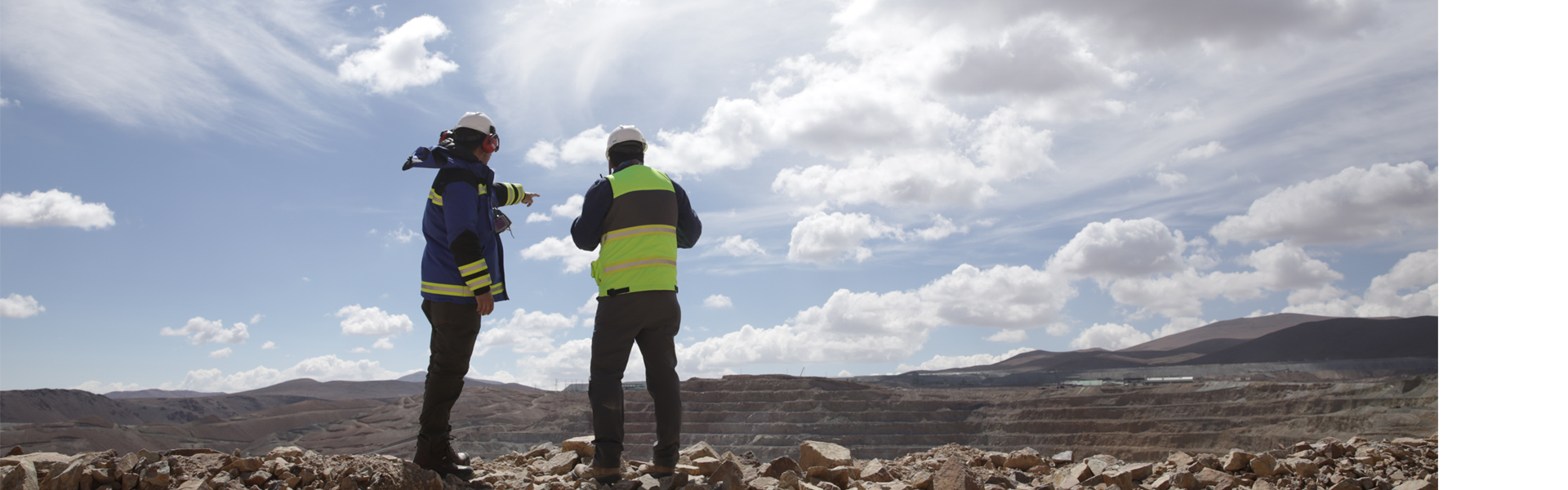 Two engineers inspect a mining site under a cloudy sky.
