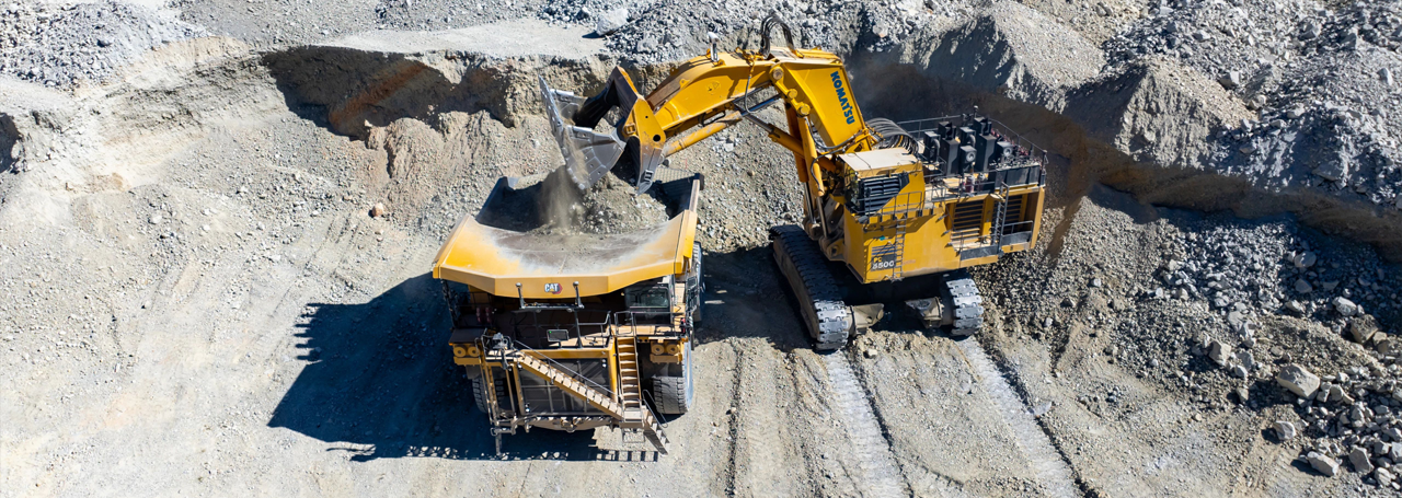 Excavator loading dirt into a large dump truck at a mining site.