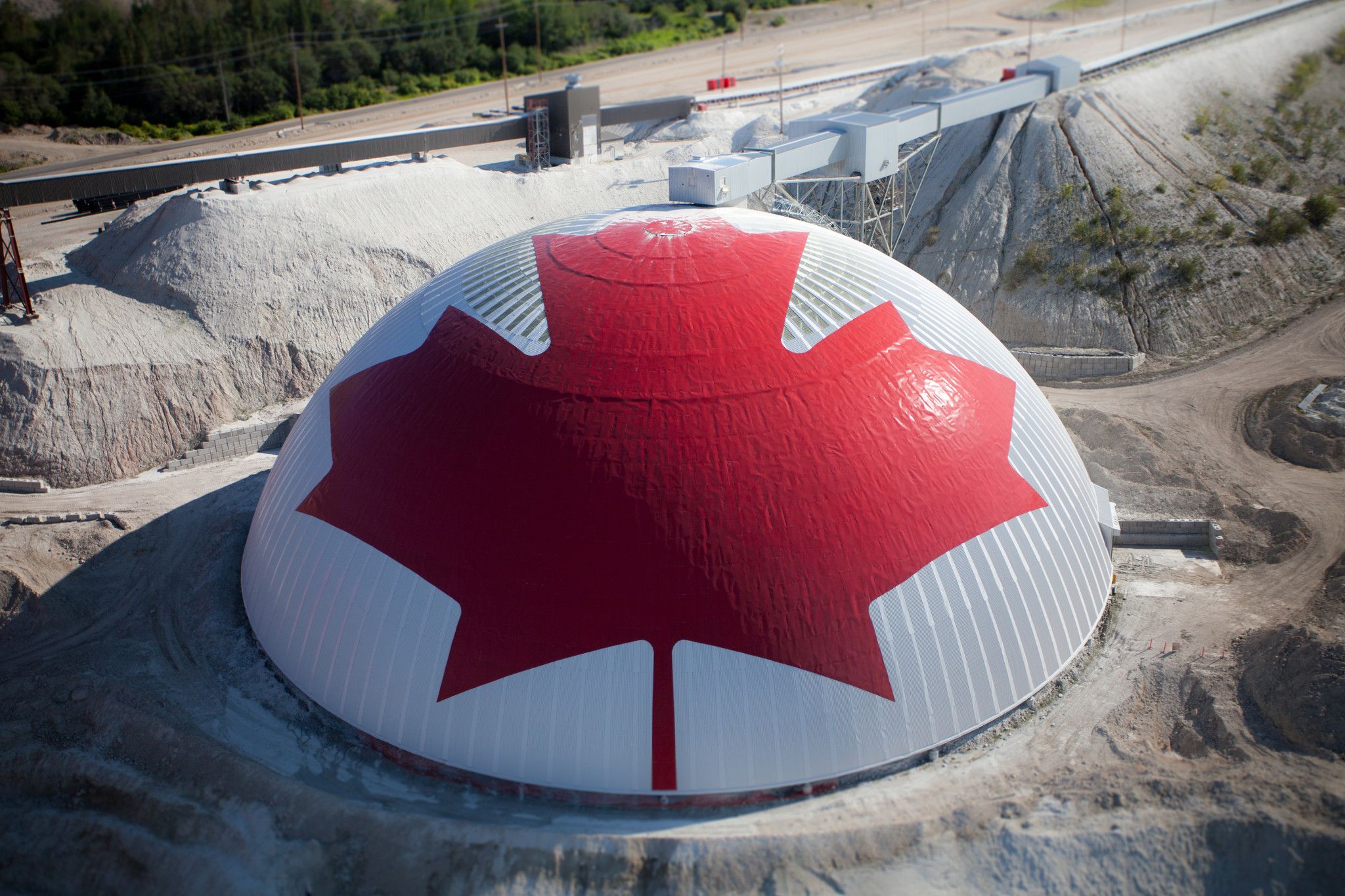 Dome with a red Canada flag pattern surrounded by industrial landscape and forest.